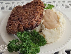 Chicken Fried Steak Tilted on top of mashed potatoes and gravy with a sprig of parsley.