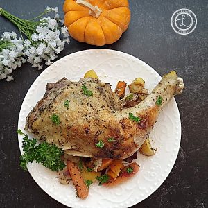 Chicken leg quarter on a plate with roasted vegetables.