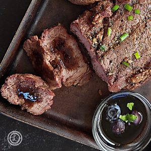 A small bowl of Blueberry Balsamic Glaze with a glazed steak in the background.