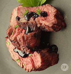 Slices of beef with blueberry balsamic glaze on top and a sprig of parsley.