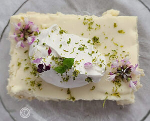 Dairy-Free Lime Cream on top of a piece of my Vegan Key Lime Cheesecake with flowers, lime zest, and sprig of mint.