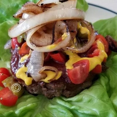 Cooked burger on lettuce, grape tomatoes, bread and butter pickles, BBQ sauce, mustard and caramelized onions