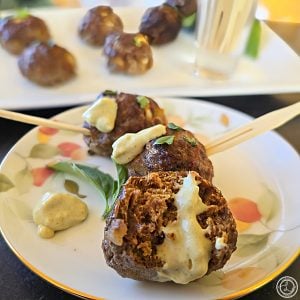 Dairy-Free Curry Dipping Sauce. Three appetizer meatballs in a row with wooden forks. More meatballs in the background.
