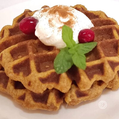 Two waffles on a plate with whipped cream, cranberries, and a sprig of mint.