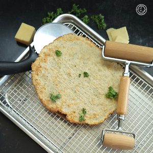 Pictured is a cooling rack and tray, pizza cutter, rolling pin, a pizza crust, with some cheese and parsley.