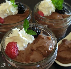 Gluten-Free Chocolate Pudding with coconut whipped cream, raspberry, blackberry, and spoon full to the side.