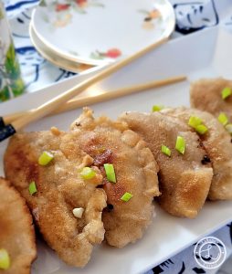 A platter of Potstickers with serving plates in the background.