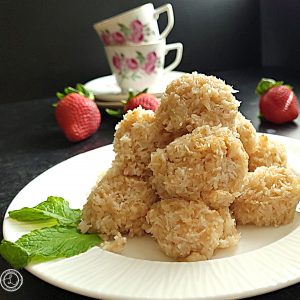 A plate of cookies with teacups and saucers in the background.