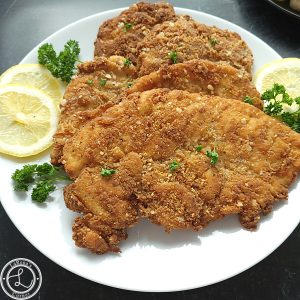 A platter of Chicken on a white plate with fresh parsley and lemon slices.