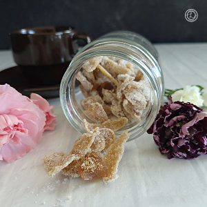 Crystalized Ginger in a jar that is tipped over with ginger spilling out. Carnations and a coffee cup are in the background.