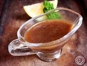 A pitcher of Quick Homemade Demi Glace with a slice of lemon and sprig of mint