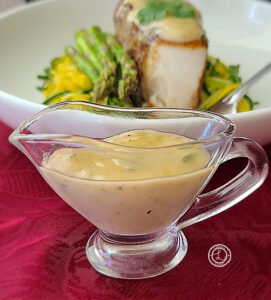 A picture of a gravy boat of Jalapeno Lime Beurre Blanc in front of a bowl of Chilean Sea Bass with some on it.