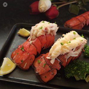 A close up of two lobster tails with a wedge of lemon and broccoli.