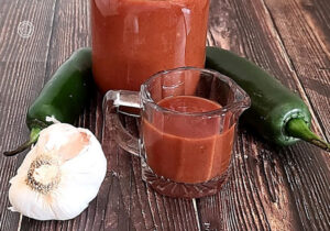 Gluten-Free Jalapeno Enchilada Sauce Recipe in a jar and in a small container with a bulb of garlic, and jalapenos so tasty