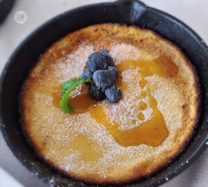 Gluten-Free Dutch Baby Pancakes a cooked pancake with mint, powdered monkfruit, blueberries, and sprig of mint.