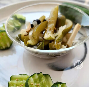 A bowl of horseradish pickles and some cut up cucumbers with mustard seeds