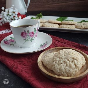 A espresso cup and saucer with a small plate of three cookies and more on a platter behind it.