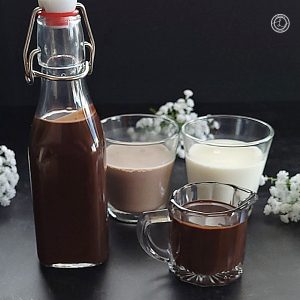 Homemade Chocolate Syrup in a bottle and in a creamer with milk and chocolate milk in the background.