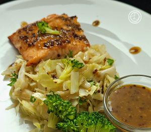 Mustard Caraway Fried Cabbage on a plate with broccoli, sauce, and salmon in the background.