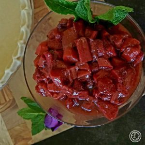 Strawberry Rhubarb Compote in a bowl with a flower, and the edge of a pie crust on the side.