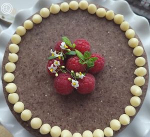 A close up of a cake with Hazelnut Marzipan Icing and decorated with white chocollate chips, raspberries and small white flowers.