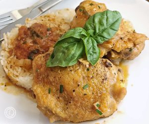 Italian Apricot chicken on a plate with rice, sauce, and a sprig of basil.