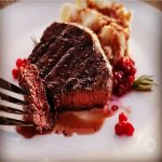 Elk Steak with Red Wine Balsamic Reduction a square picture of a steak bite cut out tilted against mashed potatoes.