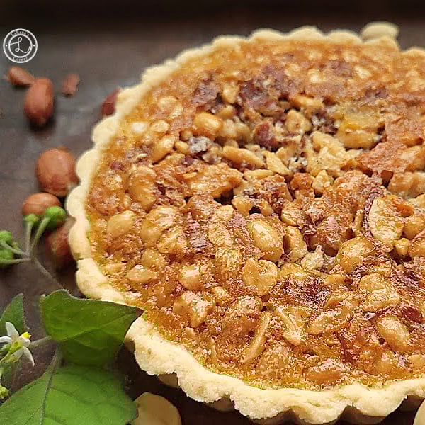 Gluten-Free Southern Peanut Pie Recipe Gluten-Free Southern Peanut Pie peeking out from the right side. with peanuts and some greenery on the left.