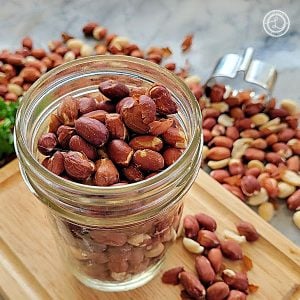 Roasted Raw Spanish Peanuts in a square photo. Nuts in a canning jar on top of a cutting board with nuts all around.