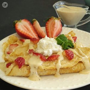 Gluten-Free Vanilla Sauce in a small pitcher in the background with vanilla stuffed crepes.