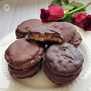 Gluten-Free Chocolate Peanut -Butter Patties stacks on a white plate with top cookie having a bite out of it. With red roses in the background.