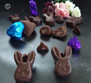 Tigernut Butter Granola Truffles bunnies, large chocolate chips, hears, and several chocolates wrapped in colorful wrappers, with flowers in the background. Two of the chocolates are cut in half.