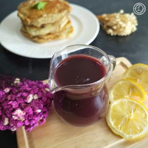 A close up of the coulis with a stack of pancakes and flowers in the background.