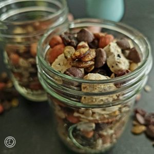 A pint size jar full of Gluten-Free Crackers trail mix. With trail mix, vase, flowers in the background.