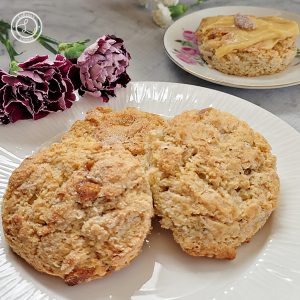 A close up of Lemon Ginger Scones with carnations and a scone with lemon curd in the background.