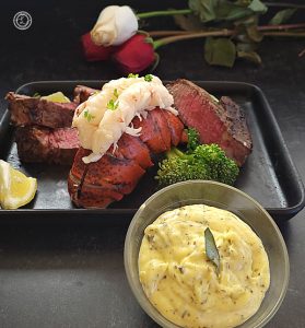 Roses in the background behind fillet mignon and lobster with Bernaise sauce in the front.