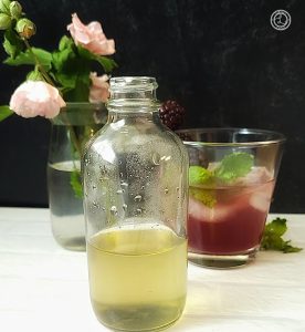 Monkfruit Mint Simple Syrup. Monkfruit Mint Simple Syrup in a bottle with a drink with mint in the background.