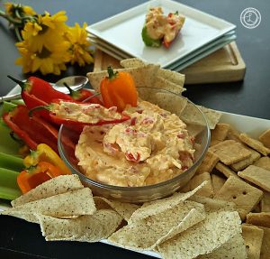 Pimento Cheese Dip in a bowl on a platter with veggies, chips, and crackers. Plates, and veggies with the dip on the plate in the background.