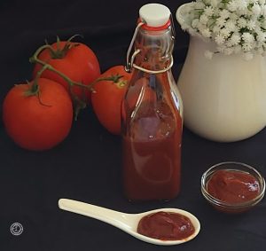Refined Sugar-Free Ketchup Bottle spoon, and small bowl of ketchup. In the background is a vase with flowers, small basket with tomatoes.