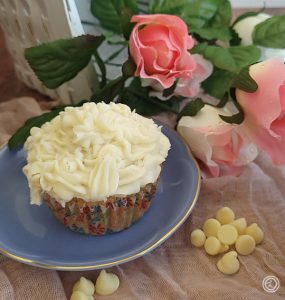 Gluten-Free Vanilla Cupcakes a cupcake on a plate with roses and white chocolate chips in the background.