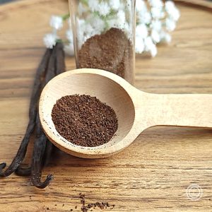 A small bottle, vanilla beans, and a tablespoon with some in it.