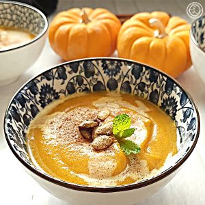 A closeup bowl of soup with toppings and mini pumpkins in the background.