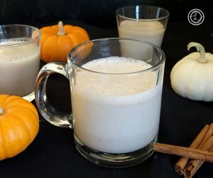 A coffee cup and drink glasses of horchata with cinnamon sticks and baby pumpkins in the background.