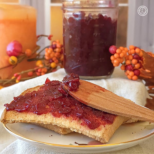 Small Batch Lingonberry Jam Recipe Small Batch Lingonberry Jam on a piece of gluten-free toast. A jar of jam, candle, and flowers in the background. The wooden butter knife has some jam on it.