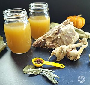Two cans of Homemade Turkey Bone Stock with turkey bones, mini pumpkin, sage leaves, and peppercorns.