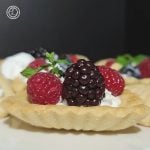 Gluten-Free Almond Cookies or tartlets a close up of one up close with whipped cream, fresh berries, and sprig of mint. Others are in the background.