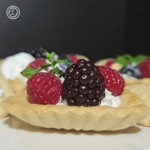 Gluten-Free Almond Cookies or tartlets a close up of one up close with whipped cream, fresh berries, and sprig of mint. Others are in the background.