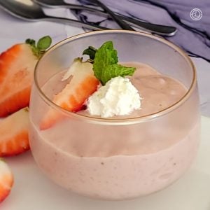 A cup of Gluten-Free Homemade Strawberry Pudding with sliced strawberries and coconut whipped cream.