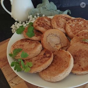Gluten-Free English Crumpets On a plate. One is opened and buttered with parsley and flowers in the background.