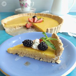 Gluten-Free Lemon Olive Oil Tart behind a slice of tart. Topped with fresh fruit and sprig of mint.